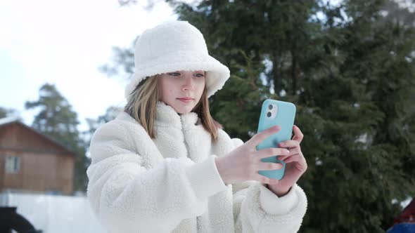 Focused Young Girl in Stylish Outfit Using Smartphone Outdoors at Wintertime alt