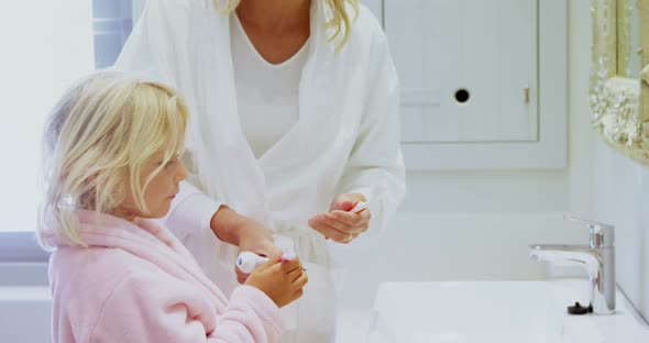 Mother teaching her daughter to brush her teeth in bathroom at home 4k