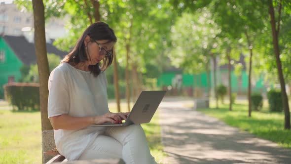 Joyful Adorable Beautiful Business Senior Woman Wearing Eyeglasses Sittingin Park Outdoors, Working alt