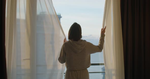 Back View of Young Woman Closing Curtains in Apartment