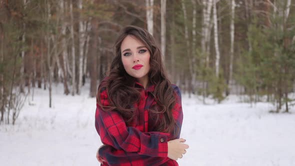 Young Woman with Wavy Hair Standing and Touching Face in Winter Forest