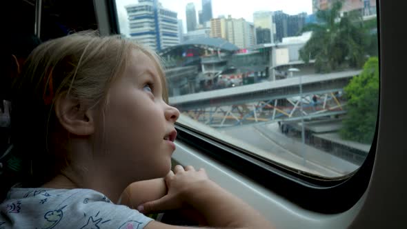 Little Child Girl Looks Out Window of Train in Carriage During Journey