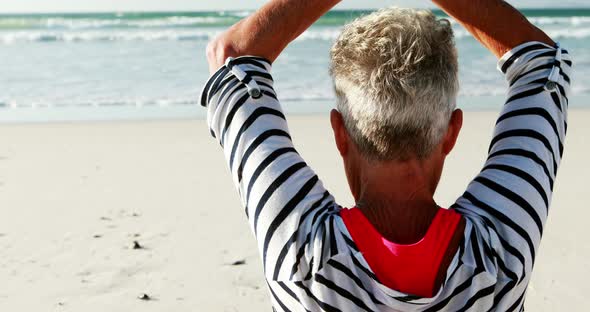 Senior woman doing yoga on the beach alt