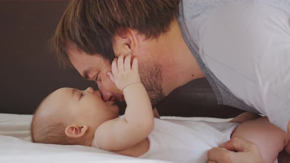 Close of Millennial Black Father Lying on Bed Playing with His Newborn Baby Dauther. alt