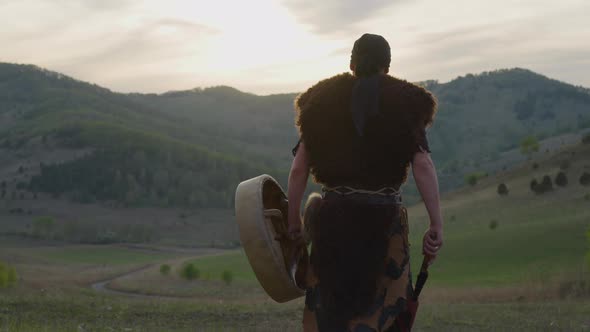 Actor Walks Carrying Shamanic Drum Against Old Hills alt