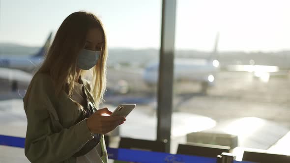 Blonde Woman in Medical Mask Uses Phone Walking Through Airport Terminal alt