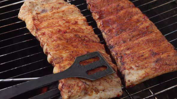 Closeup of the Delicious Spiced Ribs Rotated on the Grill with Kitchen Tongs alt