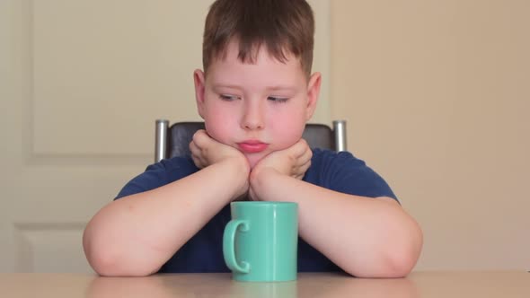 A Fat Child is Sitting at a Table with His Chin in His Hands