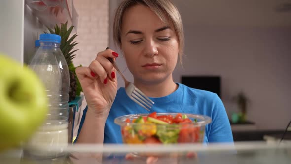 Slimming Woman Eating Tasteless Salad at Fridge alt