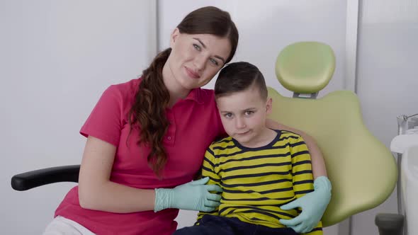Portrait of Happy Female Dentist with a Child Smiling at Camera in Dental Chair alt