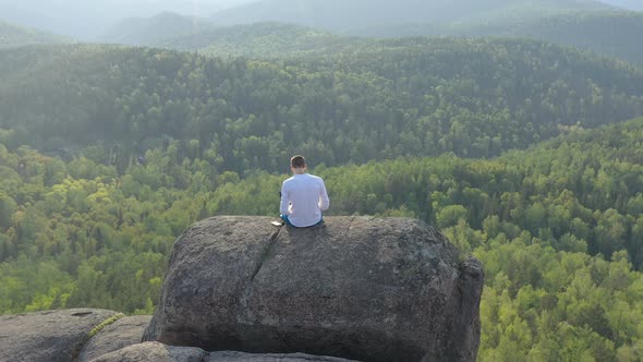 Top View of a Man with a Laptop on the Edge of a Cliff.