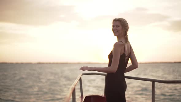 Happy Slim Girl in Black Dress Looking at Sunset During Ferry Trip Across Sea alt