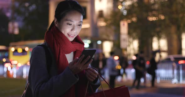 Woman use of mobile phone and hold shopping bag in city at night alt