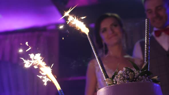 Sparklers on the wedding cake, bride and groom in the background alt