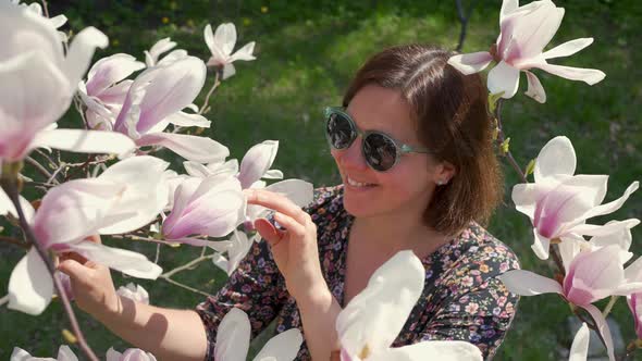 Happy Woman Enjoying Nature and Touching Blooming Magnolia Flowers in the Garden