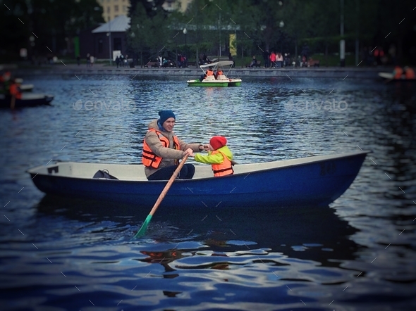 Father and son sail on a boat with oars on the lake in the park.