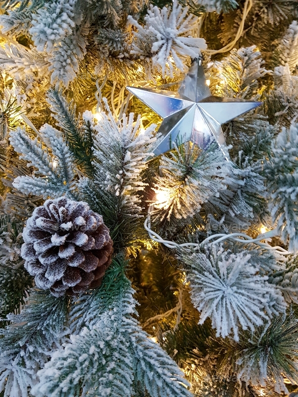 Silver star on an artificial Christmas tree with snow and pine cones