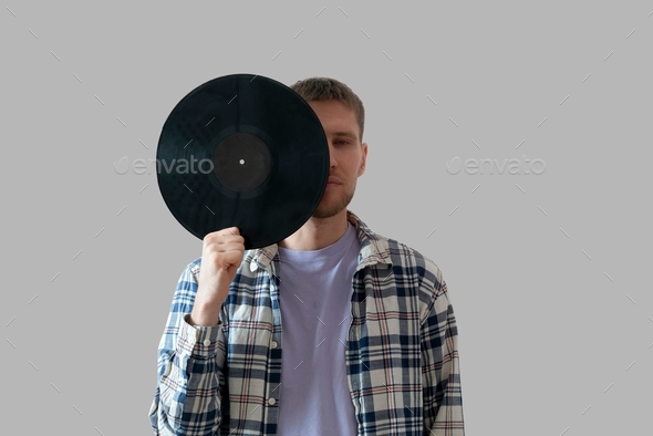a male music lover holding a black vinyl record and cover his face