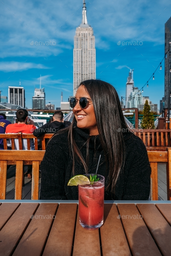 portrait of woman smiling wearing jumper in New York City rooftop bar with Empire State Building