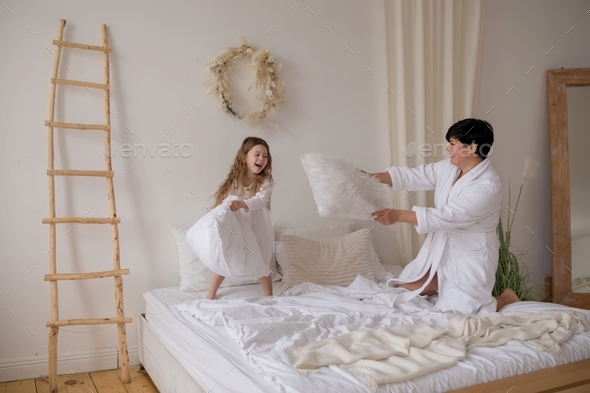 Mom and daughter have fun pillow fight on the bed