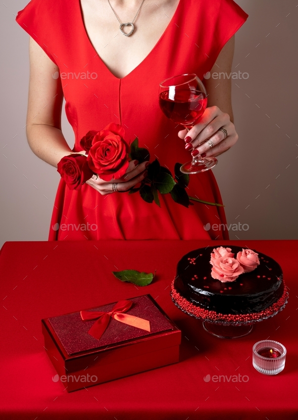 Woman in red dress hand holding a red rose and wine glass. Romantic candlelight dinner.