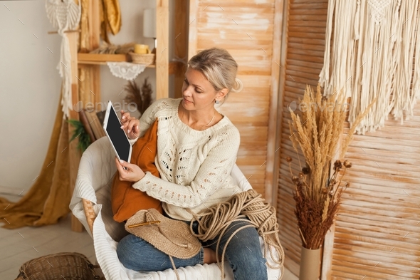 Woman in a cozy interior with knitting jute using a laptop for needlework.