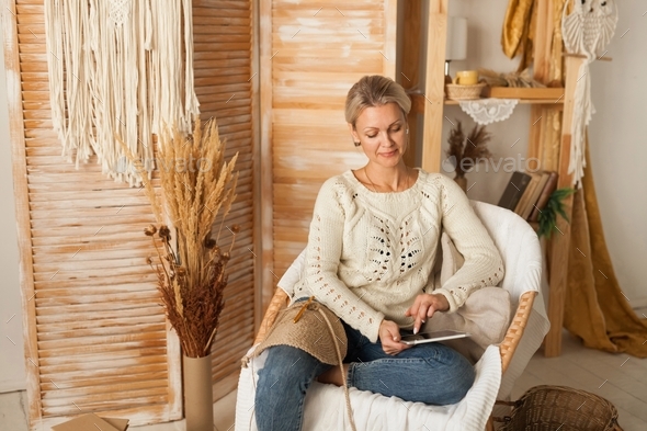 Woman in a cozy interior with knitting using a laptop for needlework.