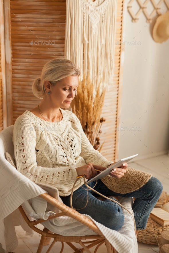 Woman in a cozy interior with knitting jute using a laptop for needlework.
