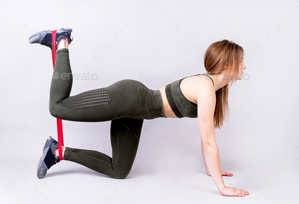 Young beautiful sportswoman working out with rubber resistance band training her legs