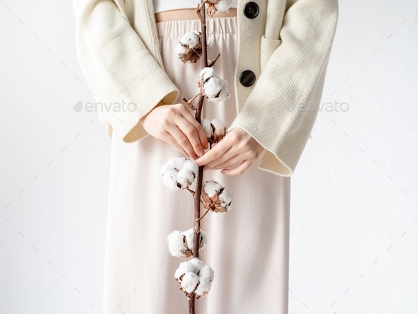 Beautiful woman in cozy clothes holding branch of cotton flowers