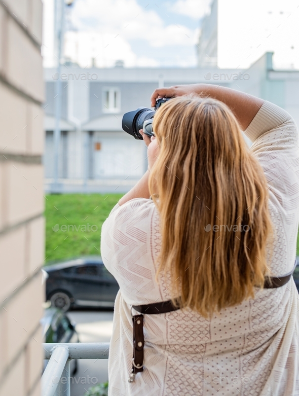 Body positive. Portrait of plus size woman taking pictures with a camera outdoors