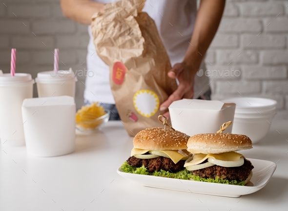 Woman in home clothes unpacking food home delivery wit burgers, noodle boxes and drinks