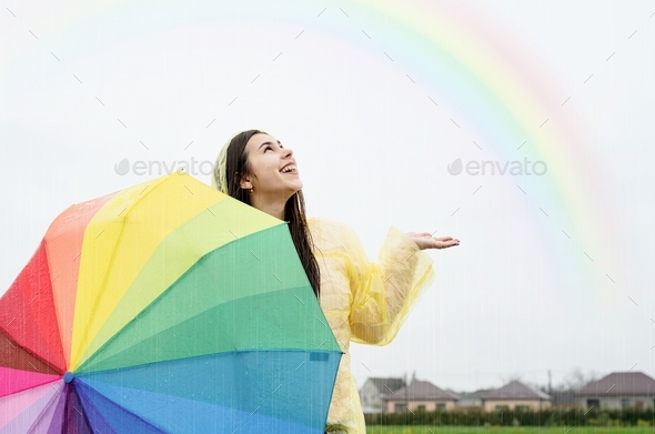 Happy woman in raincoat holding umbrella and catching the rain