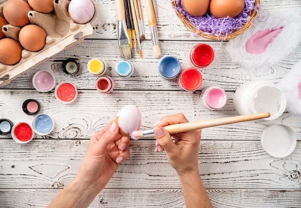 Female hands coloring easter eggs with pastel paints, top view flat lay