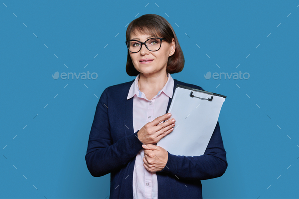 Middle age business woman with clipboard looking at camera on blue background - Stock Photo - Images