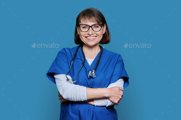 Portrait of middle aged doctor in uniform looking at camera on blue background - Stock Photo - Images