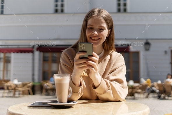 woman using phone social network chatting with friends in summer cafe