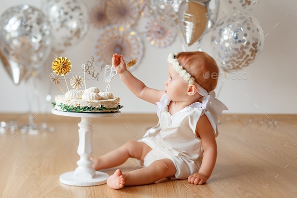 Little curly baby girl sitting on floor near her birthday cake