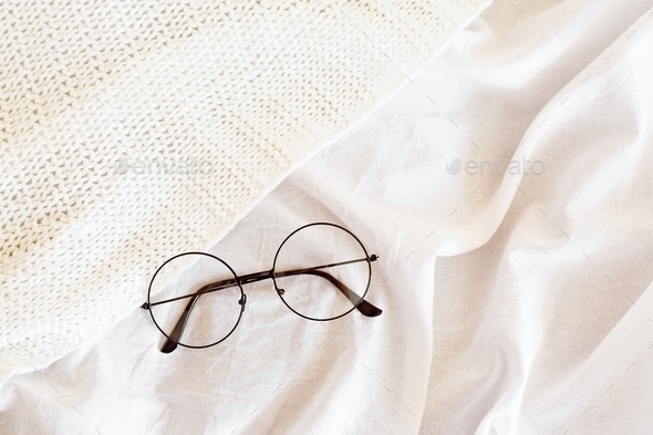 Round eyeglasses on white bedsheets and knitted blanket