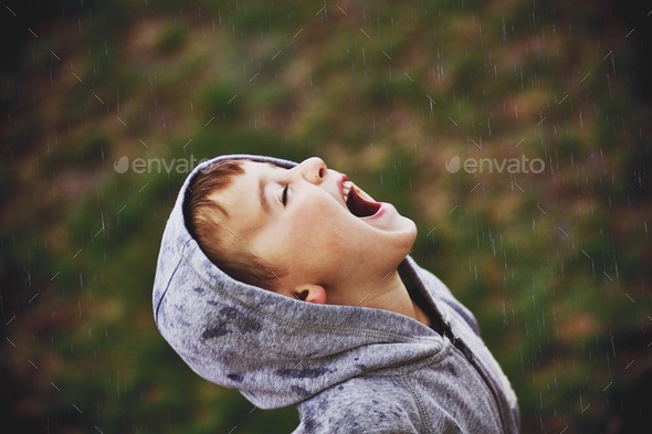 Young boy in the rain opening mouth hoping for rain drops in come into mouth!