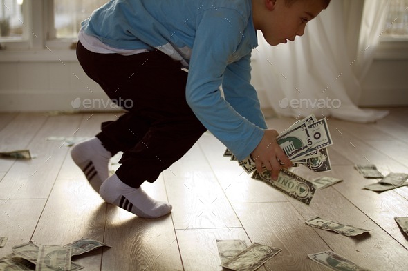 Little boy picking up fake money off the ground. A lot of toy money.
