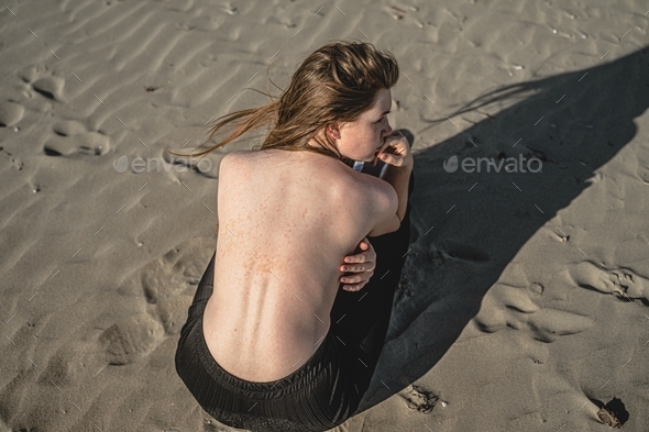 girl with age spots on her back sits on the sand