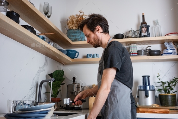 A man does housework. A young man washes dishes in the kitchen in a Scandinavian design