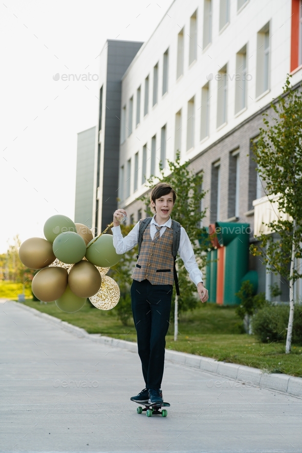 Happy High schooler with backpack and balloons go to school on skateboard on the First day of school