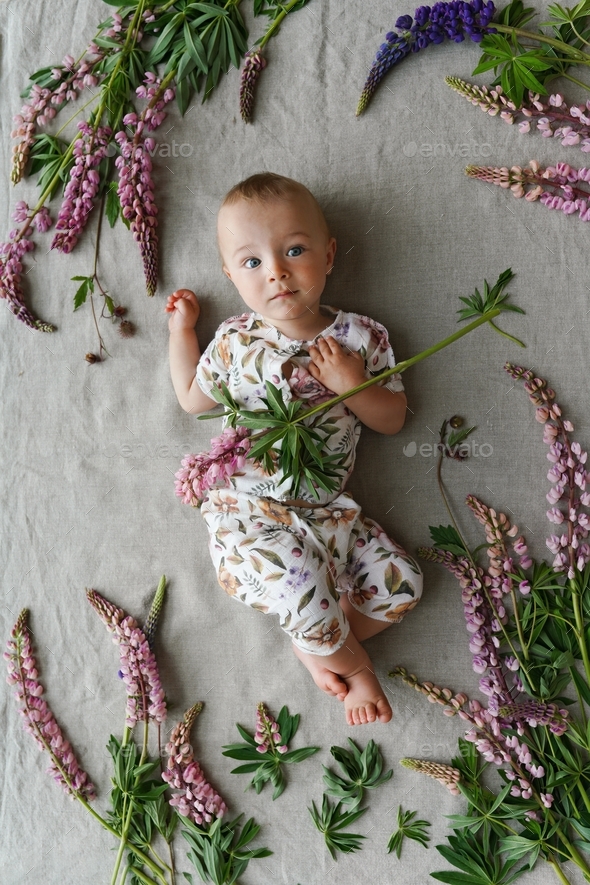 The cutest baby in calico clothes with floral print lying on linen textile blanket with pink lupins