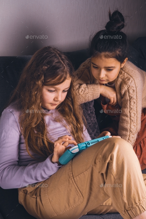 Two preteen girlfriends are actively playing video games on the console ...