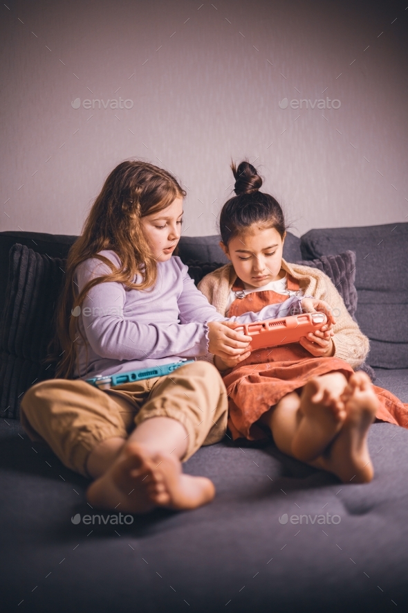 Two preteen girlfriends are actively playing video games on the console ...