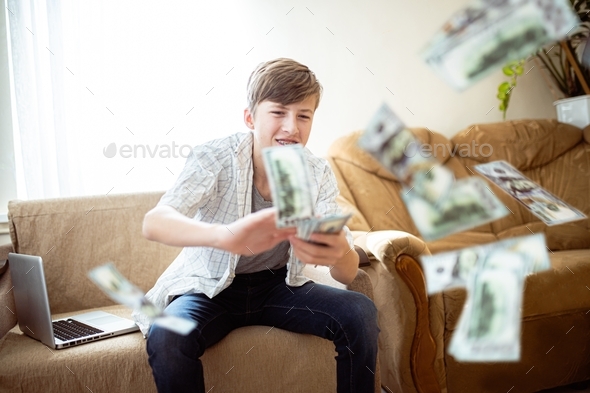 Generation z teenager wastes money by scattering it while gaming on laptop
