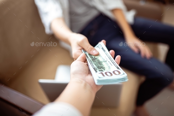 The mother gives her son a bundle of dollars. The client pays for the work by handing over money