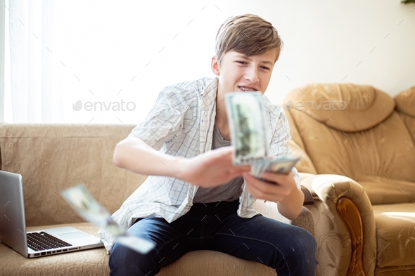 The teenager wastes money. Boy happily scatters banknotes